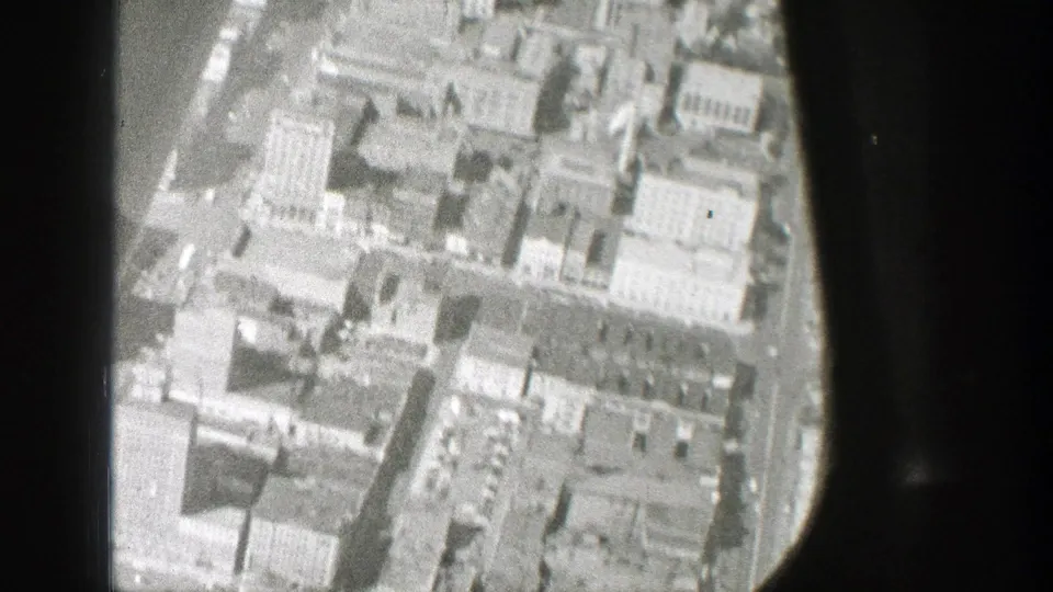 1939 8mm aerial view over dense city blocks, framed by the dark edge of an airplane window.