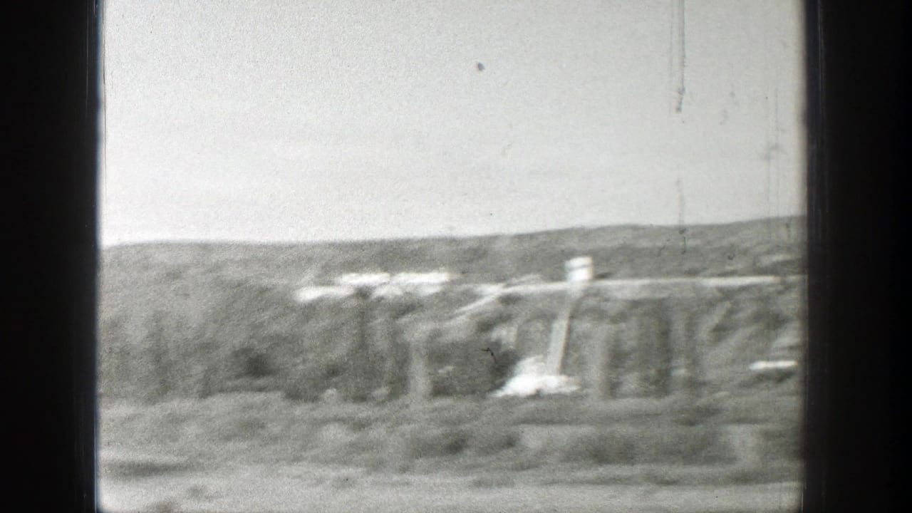 Distant concrete dam structures seen through dark window bars in a forested valley.
