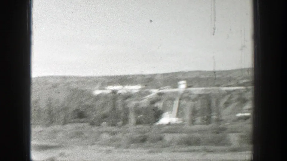 1939 Wyoming home-movie frame showing a distant concrete dam or utility structure across a wooded valley, viewed through dark window divisions.