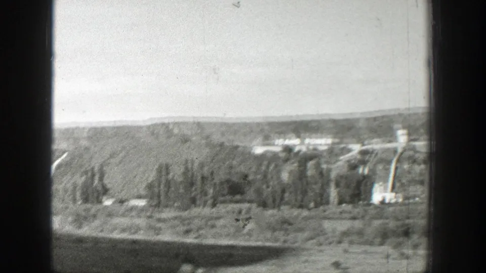 Distant dam or hydroelectric works in a wooded Western valley, with the view partially blocked by a dark vertical window frame.