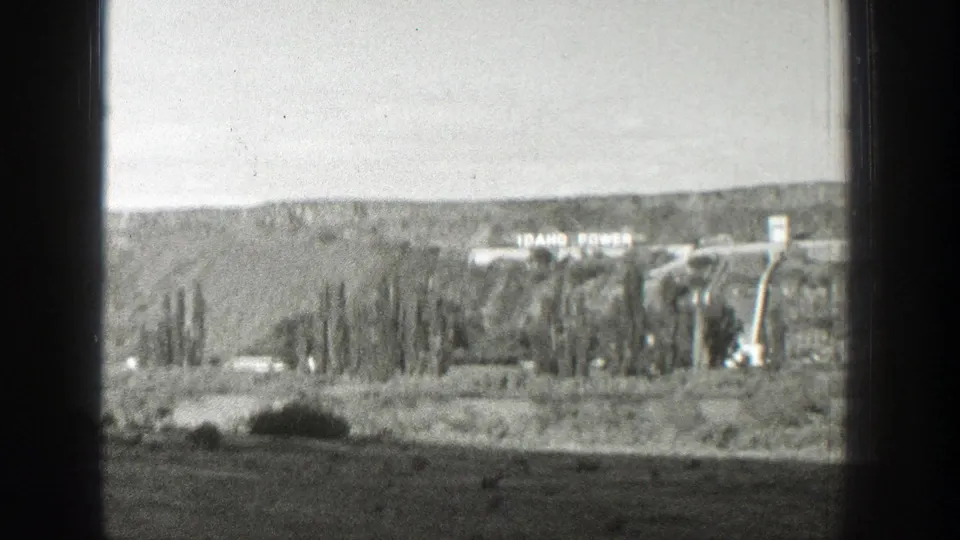 Distant view of a dam or hydroelectric site with Idaho Power lettering, filmed from a moving window in 1939 Wyoming home-movie footage.
