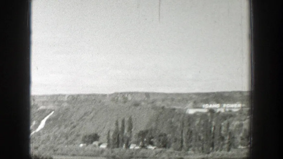 1939 Wyoming landscape frame showing a sloped hillside, a pale road or hillside cut, trees, and distant Idaho Power lettering.