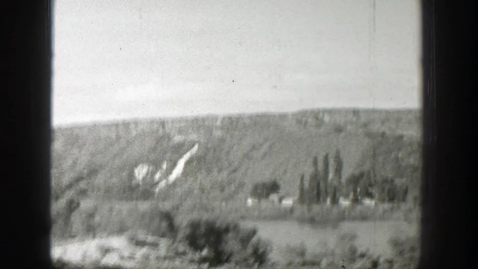 Soft 1939 Wyoming home-movie frame of valley trees below a broad hillside with pale rock or road cuts.