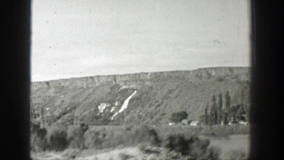 1939 Wyoming 8mm frame of a wide hillside above a valley, with tall trees and pale marks on the slope.