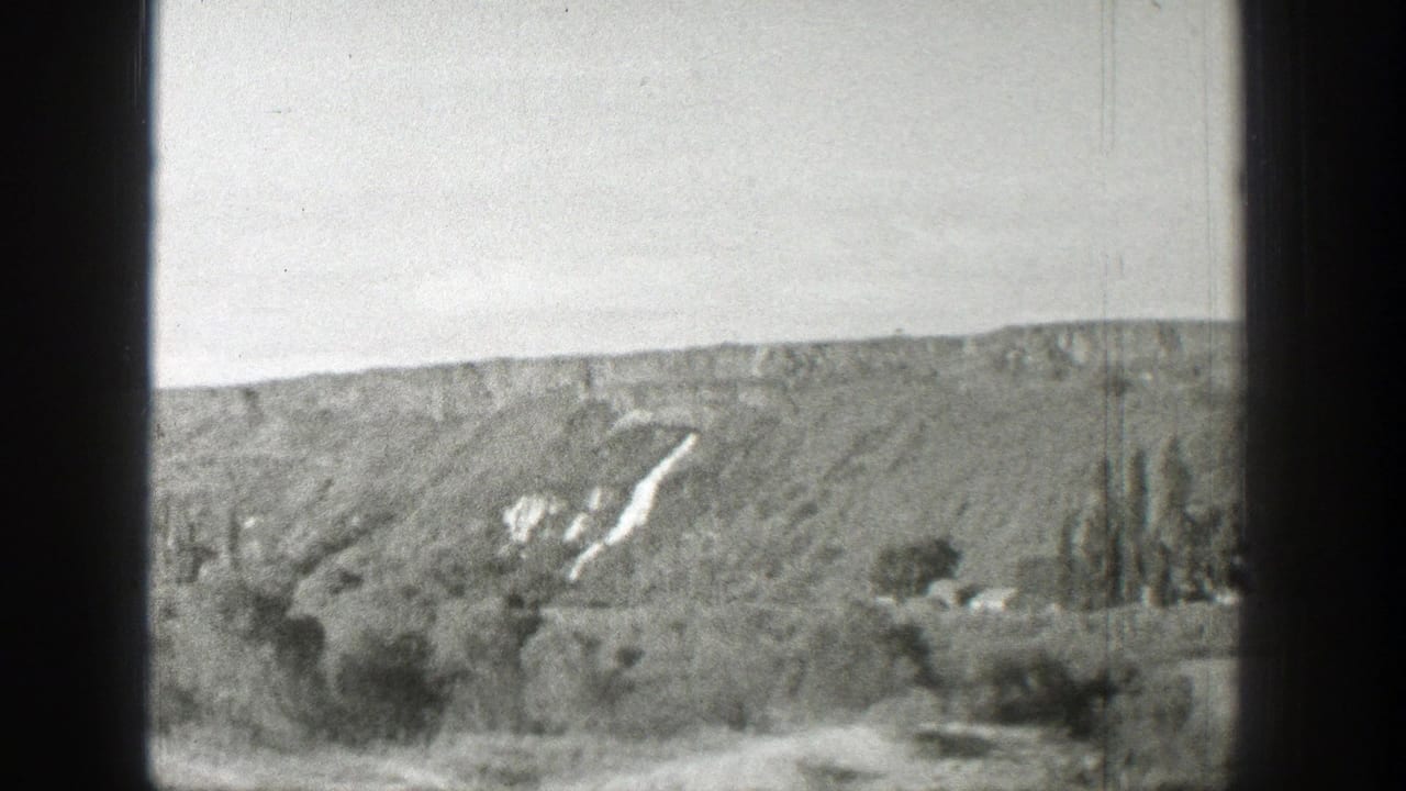 Hillside landscape seen through dark vehicle edges with pale sky and sparse trees.