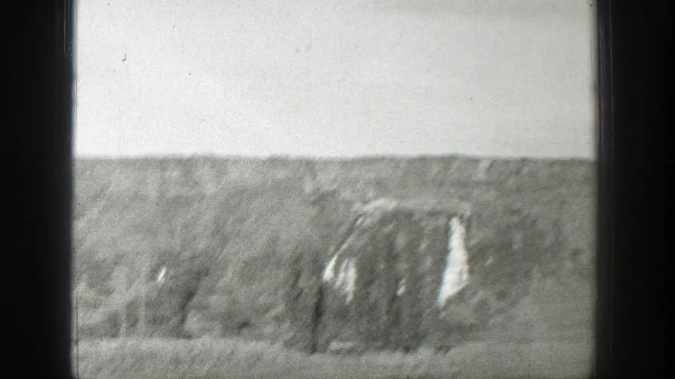 Soft 8mm frame of the Wyoming hillside and roadside trees, with a dark vertical vehicle edge cutting through the moving view.