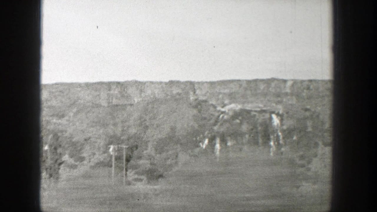 Rugged eroded canyon terrain with trees and film frame borders.