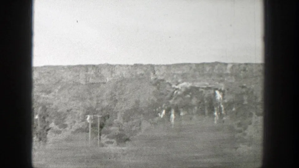 Black-and-white 1939 Wyoming home-movie frame showing eroded canyon terrain, scattered trees, pale sky, and visible 8mm film borders.