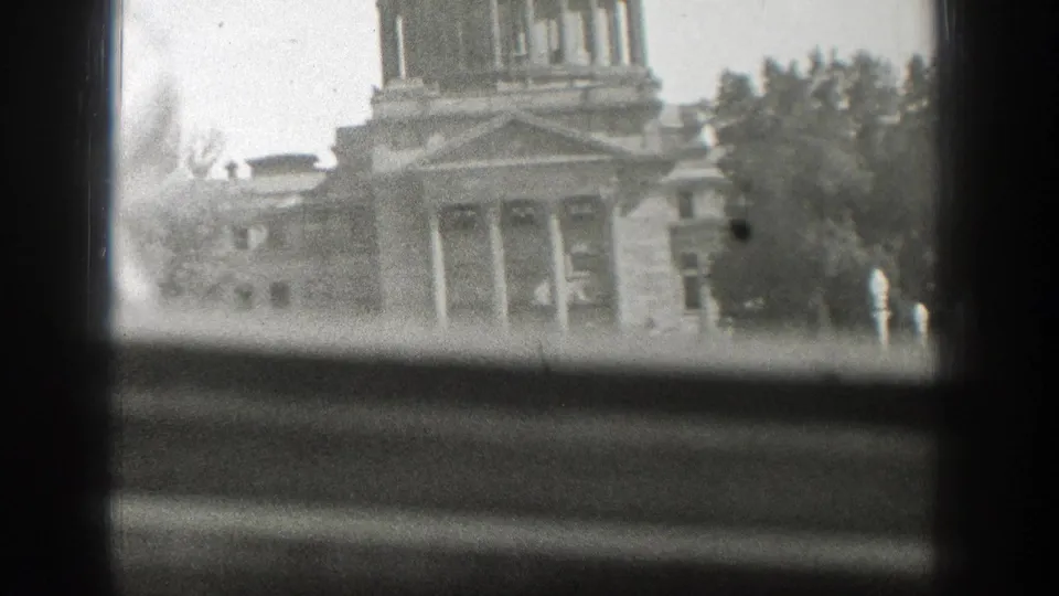 Cropped 1939 8mm view of the Wyoming State Capitol through window mullions, with the dome and entrance partly obscured.