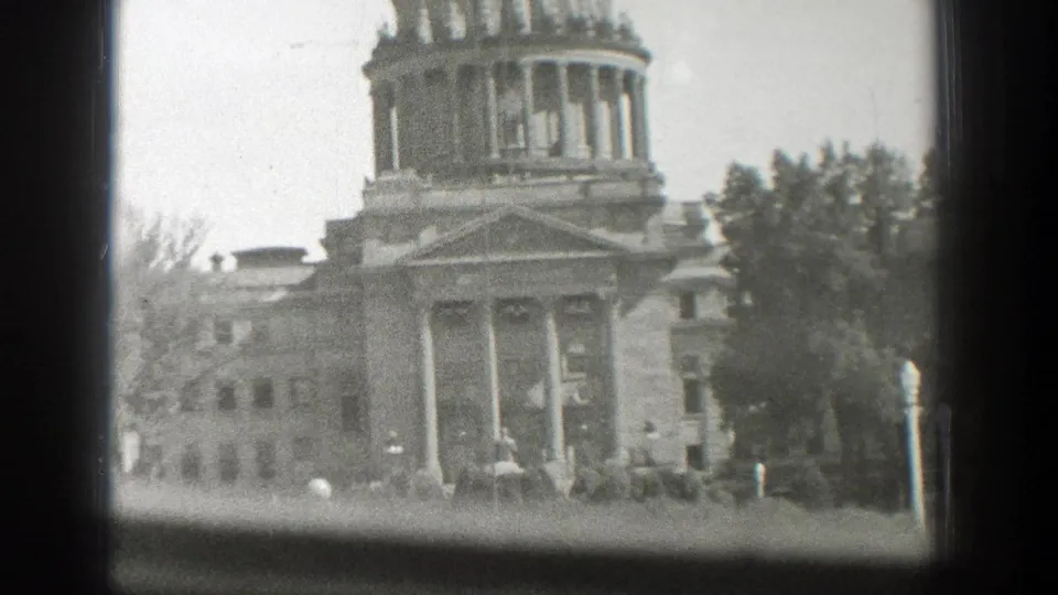 Black-and-white 1939 8mm frame showing the Wyoming State Capitol facade, dome, columns, trees, and window edge.