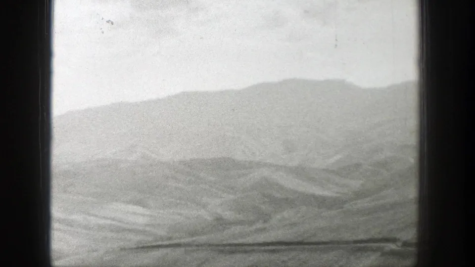 Soft black-and-white 8mm view of Wyoming hills and a broad valley, with visible film wear and frame edge shadow.