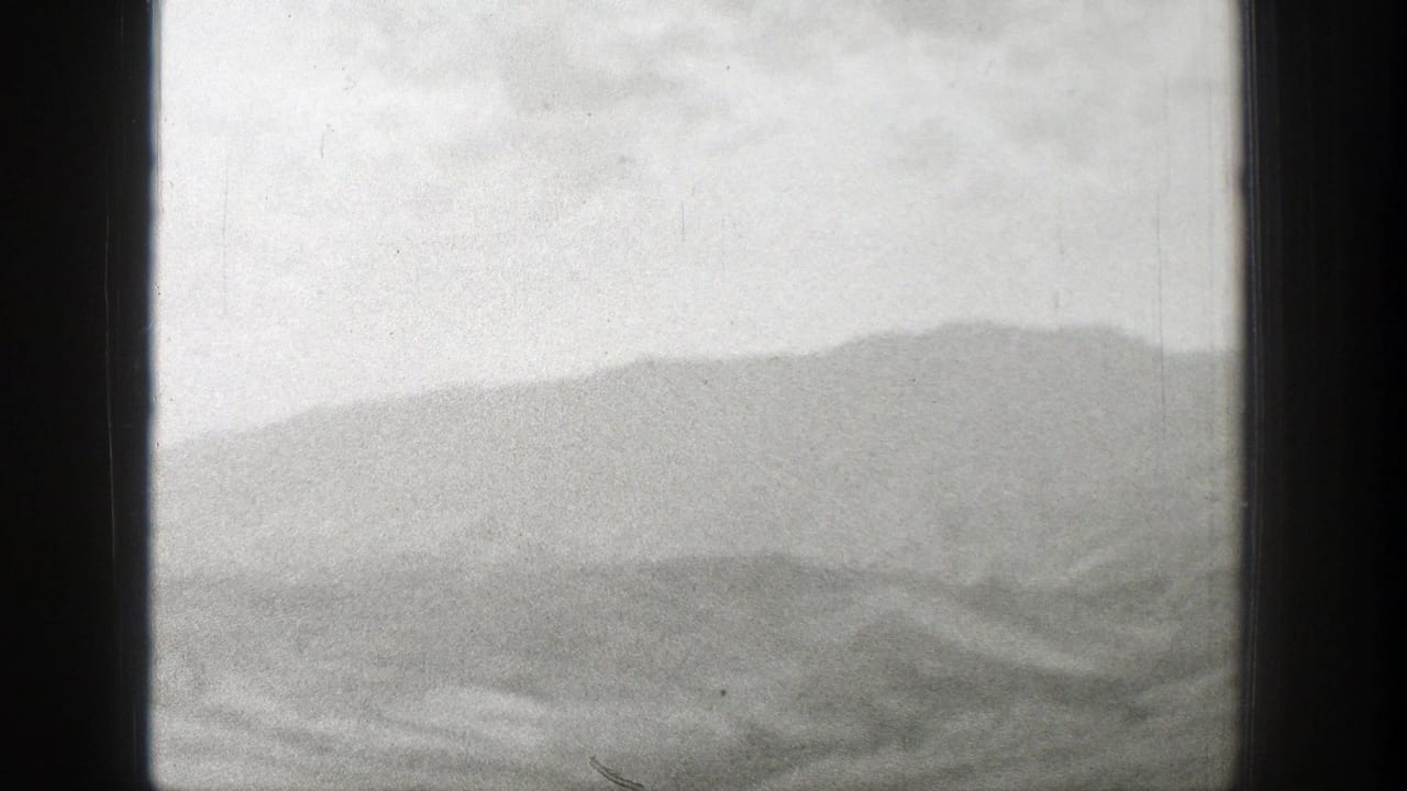Train-window view of pale sky, dry hills, and distant mountains in soft focus.