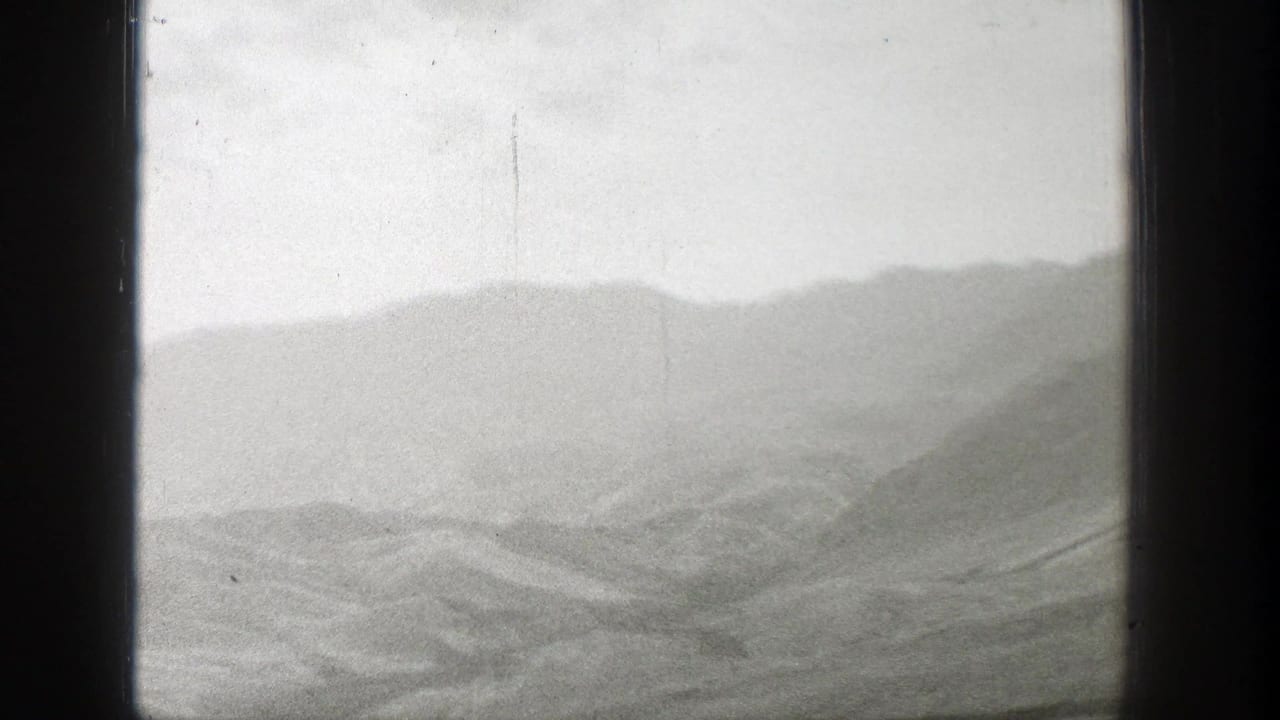 Misty mountain ridges under a pale cloudy sky, bordered by dark film edges.