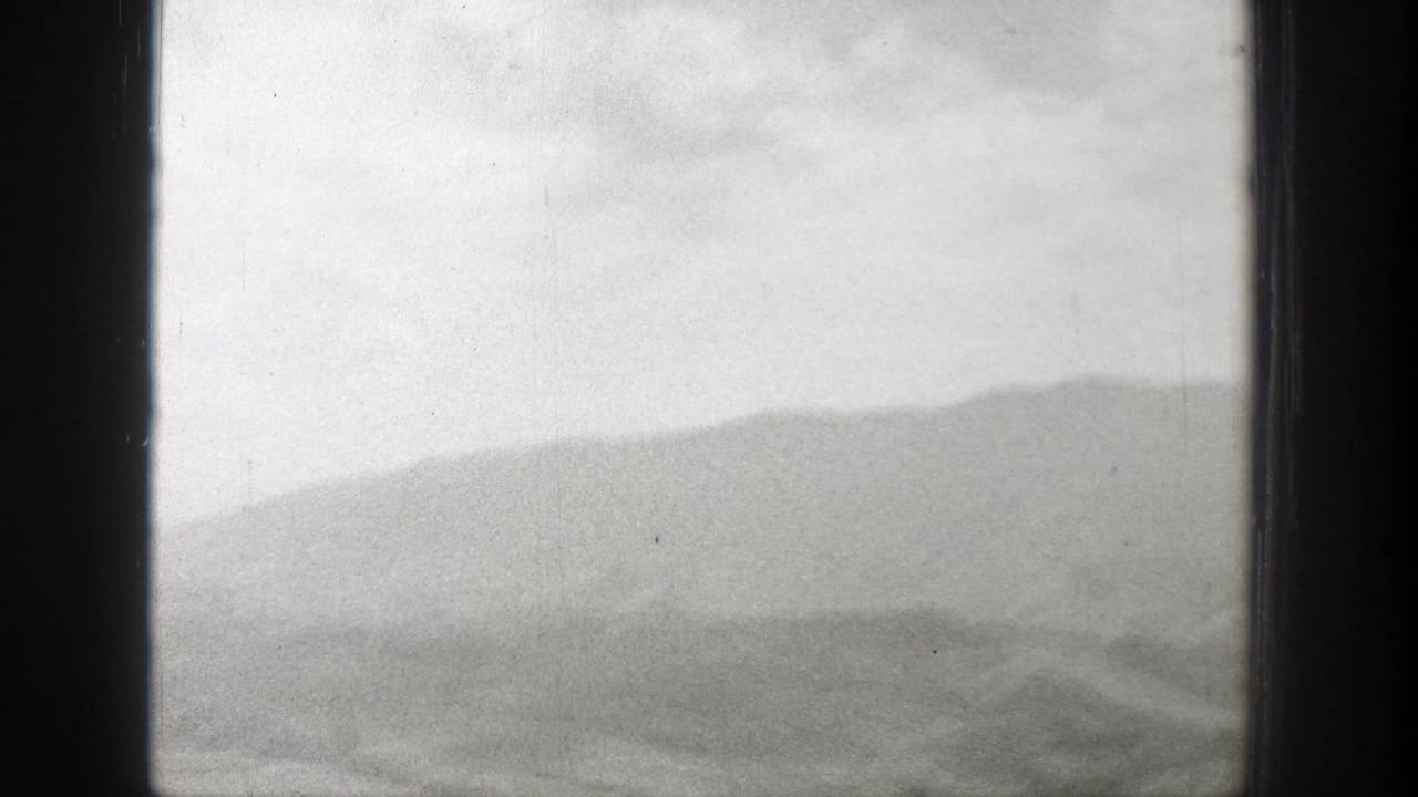 Distant hazy mountain range and overcast sky seen through dark film-frame borders.
