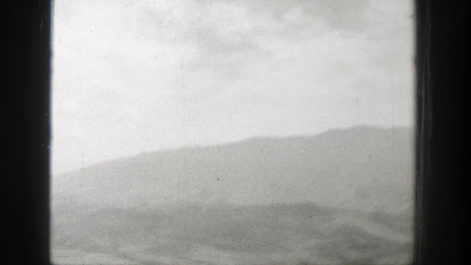 Hazy Wyoming mountain range appears beyond soft foreground terrain in a black-and-white 8mm home-movie frame.