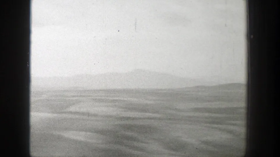 Black-and-white 8mm view of open Wyoming terrain with low hills and a hazy valley under cloud cover.