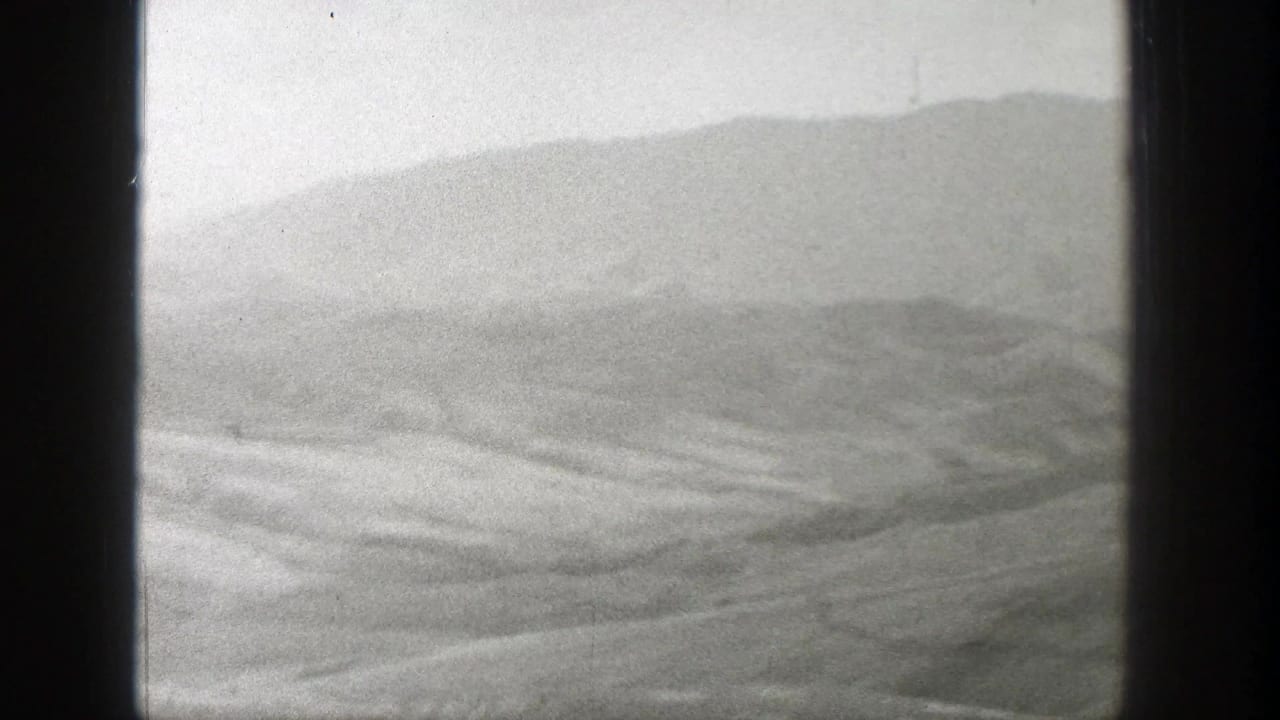 Hazy mountain ridge above a barren, undulating plain framed by dark film edges.