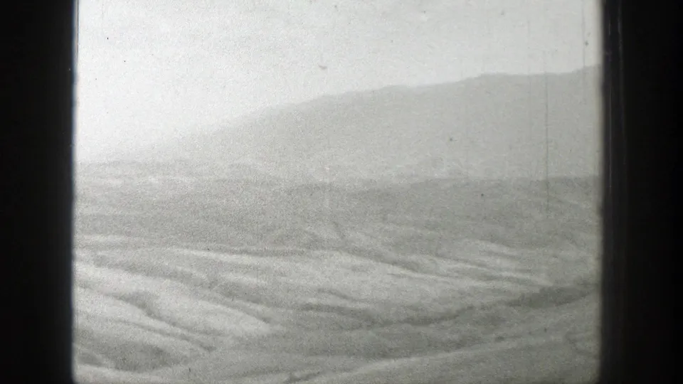 1939 Wyoming 8mm frame with layered dry ridges in the foreground and a hazy mountain mass behind them.