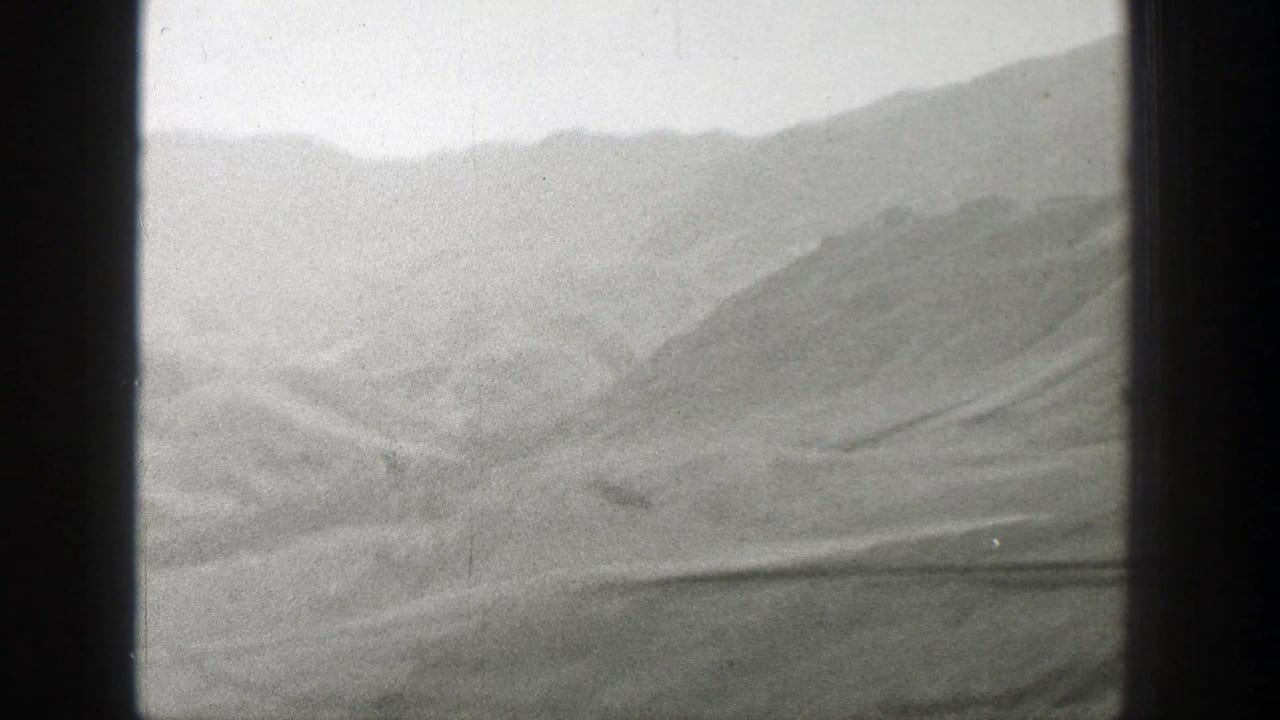 Distant hazy mountains and desert terrain seen through a dark window frame.