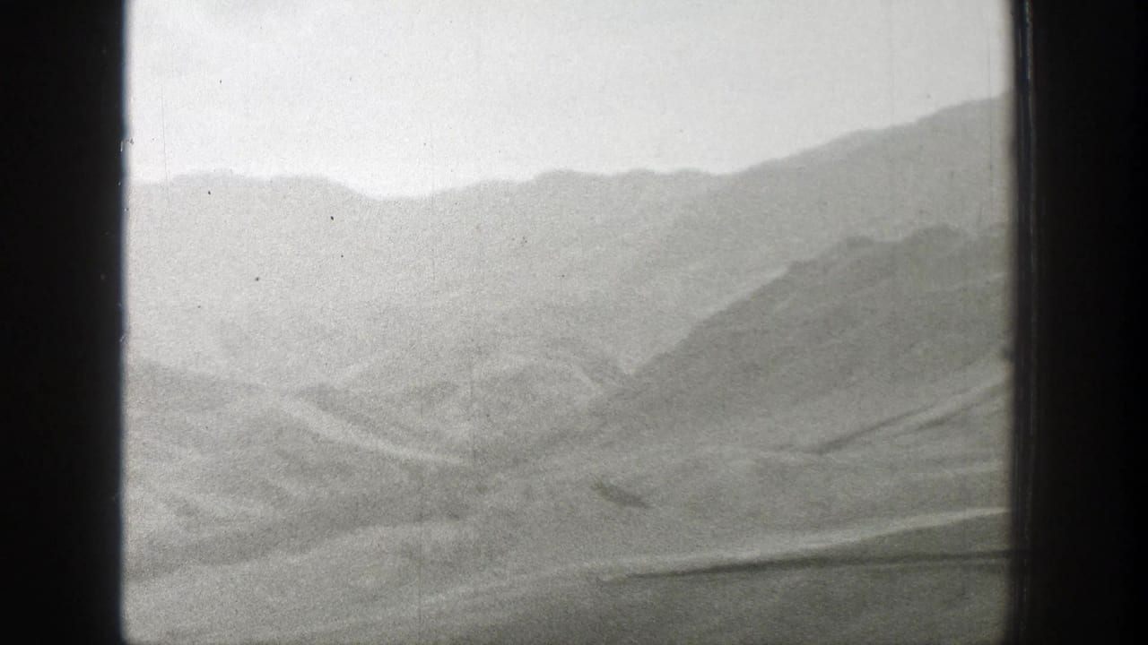 Mountain slopes and desert flats viewed through a divided window opening.