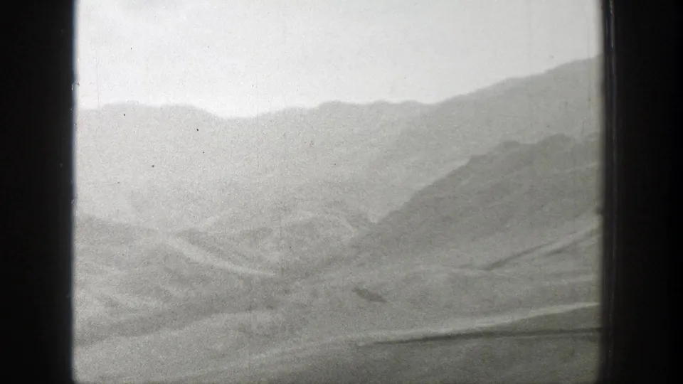 Monochrome 8mm frame of Wyoming mountain slopes and desert flats seen from behind a dark window divider.