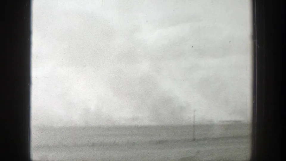 1939 Wyoming home-movie frame showing a flat rural landscape, overcast sky, sparse ground, and a distant utility pole.