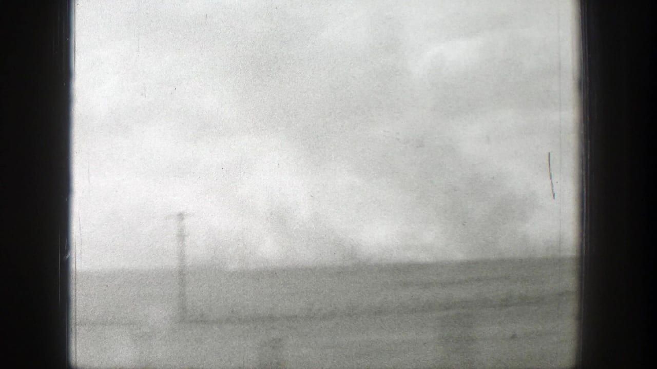 Distant utility pole and low horizon across a hazy open field beneath cloudy sky.