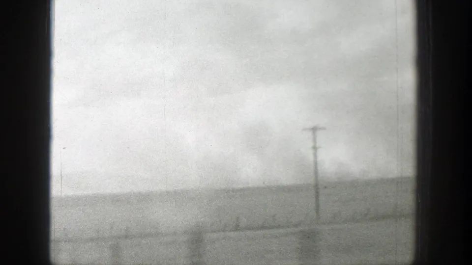 1939 Wyoming home-movie frame with a foreground utility pole, faint road or track lines, and open land under clouds.