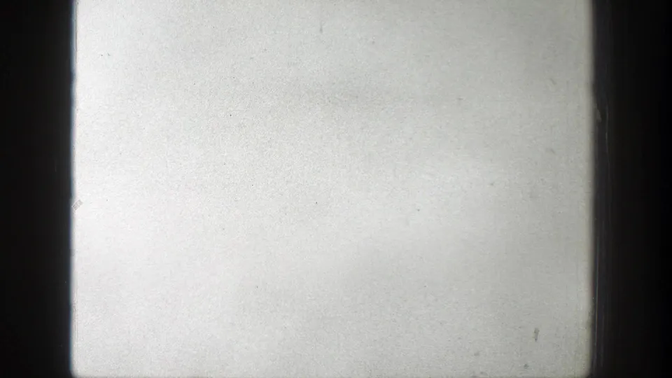 Black-and-white 8mm frame from the Wyoming wildfire clip, mostly pale sky with a faint horizon and dark edge framing.
