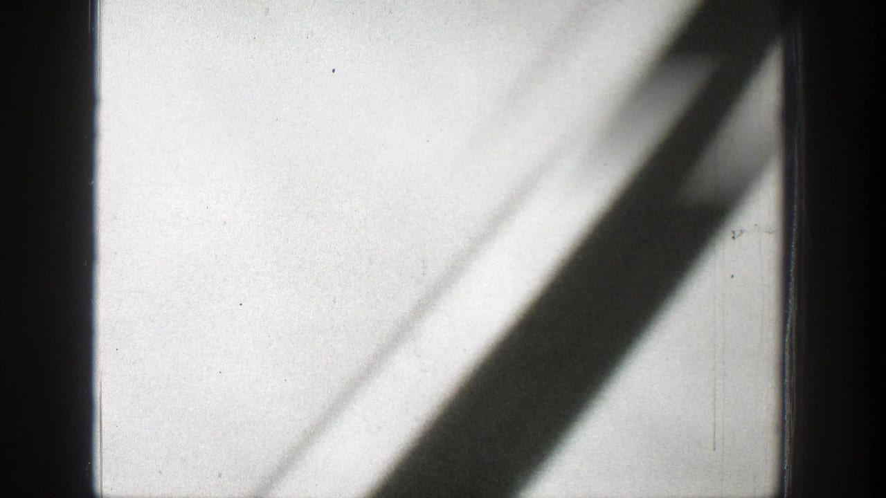 1939 Wyoming 8mm frame with dark vertical bars, diagonal shadows, pale sky, and soft smoke haze.
