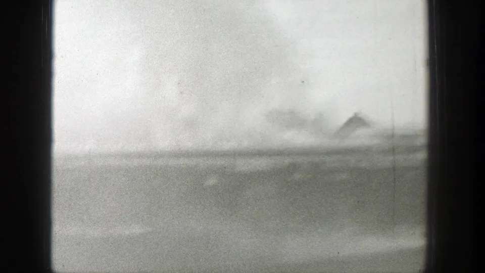 A 1939 Wyoming 8mm frame shows smoke drifting over a low rural horizon, with a faint roofline or structure in the distance.