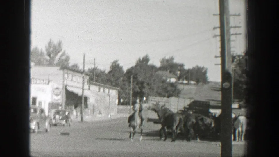 1939 Wyoming town street with men on horseback, parked cars, utility poles, and low commercial buildings.
