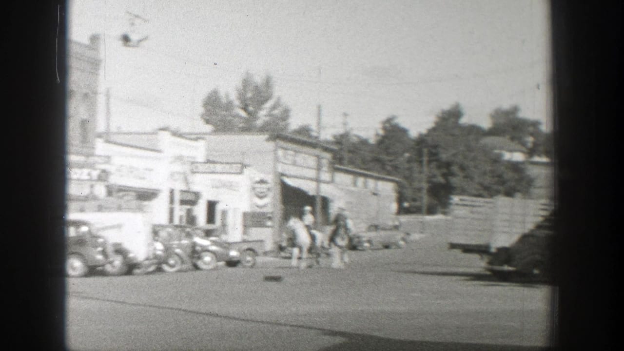 A Wyoming small town street scene shows horseback riders near vintage cars and a Chevrolet storefront in black-and-white 8mm footage.