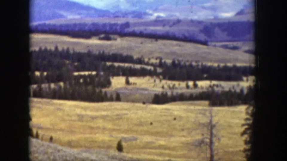 1939 Wyoming home-movie view of rolling open hills, evergreen stands, and distant mountains beneath clouds.