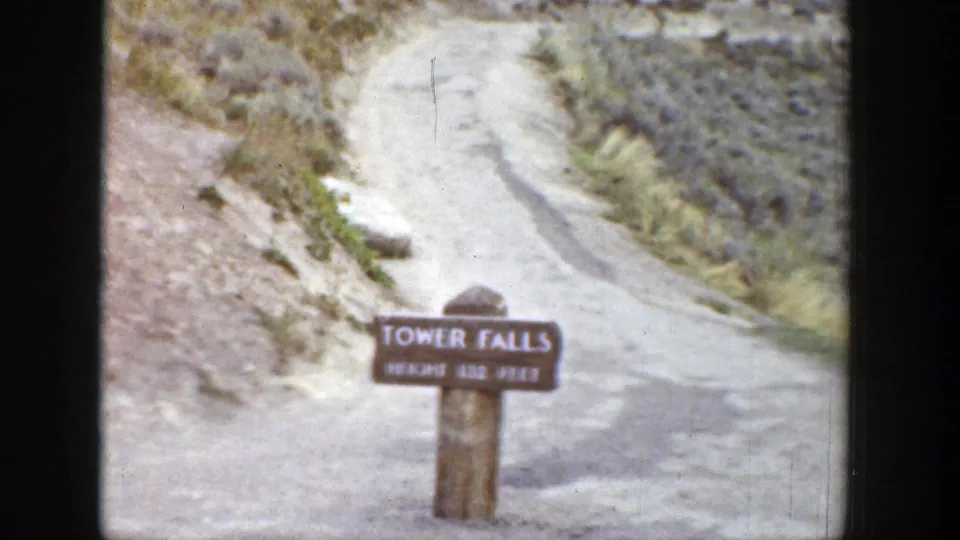 1939 Wyoming frame showing the Tower Falls height sign near a curving dirt path and dry hillside.