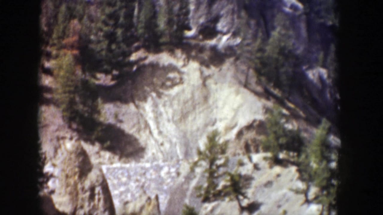 Closer view of pale rock formations and scattered evergreens in bright daylight.
