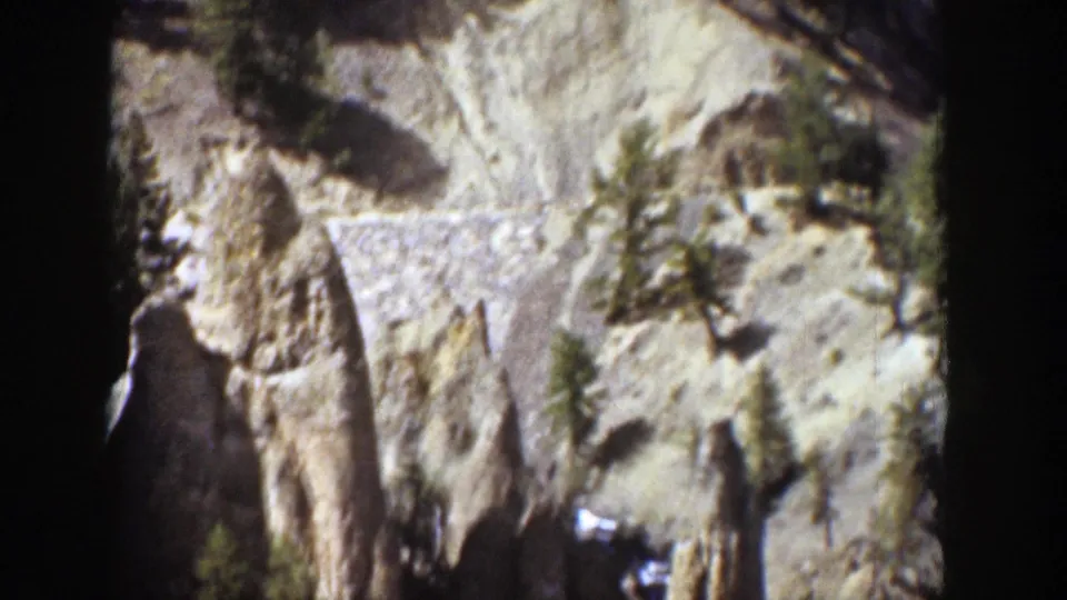 1939 Wyoming 8mm frame showing a steep cliff wall, vertical rock forms, evergreens, and high-contrast sunlight.