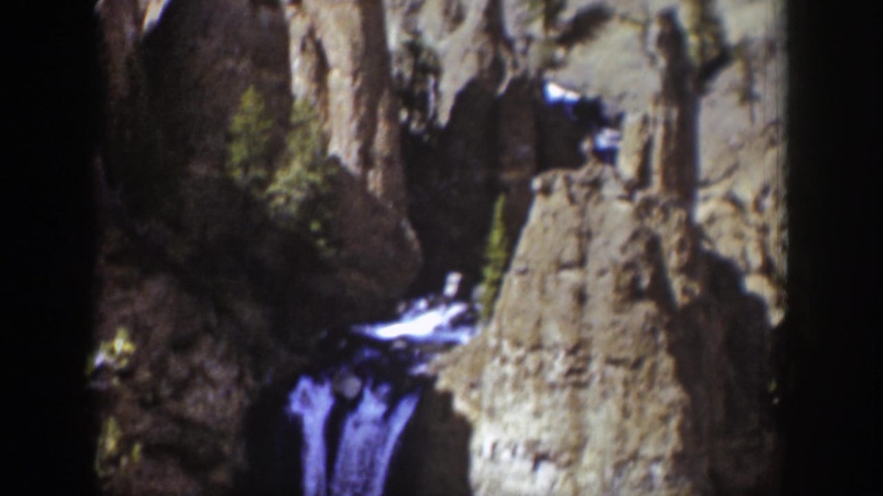 1939 Wyoming 8mm frame showing a mountain waterfall partly obscured by rugged rock walls and deep canyon shadow.