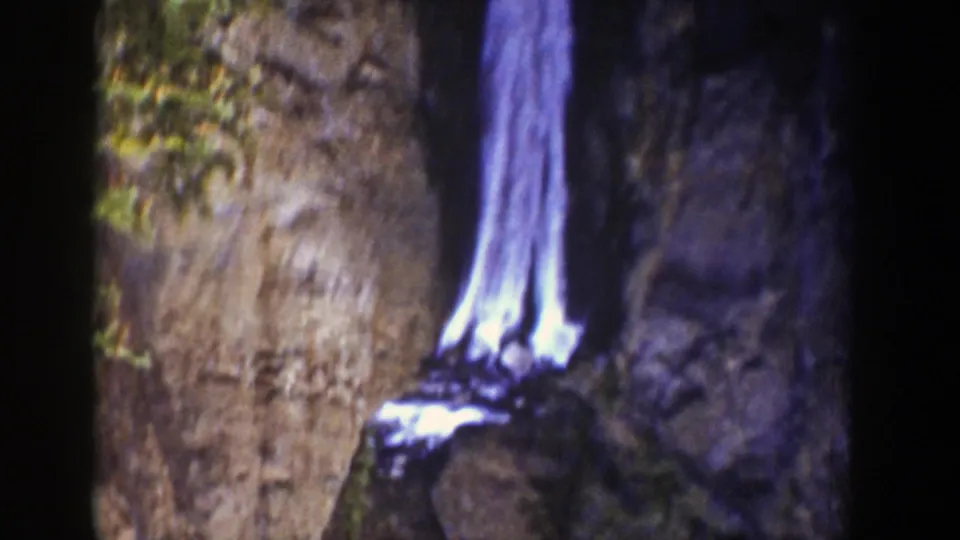 Wyoming 8mm frame from 1939 showing a bright waterfall dropping along a cliff face and foaming over rocks at the base.
