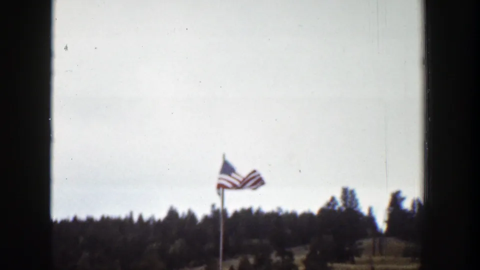 American flag waving on a pole above a treeline, filmed as a brief outdoor cutaway in the 1939 Wyoming home-movie clip.