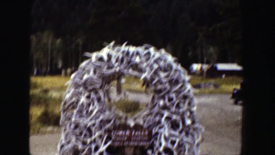 Antler arch structure stands near a roadway at Tower Falls Ranger Station in Wyoming, with forest and small buildings visible behind it.