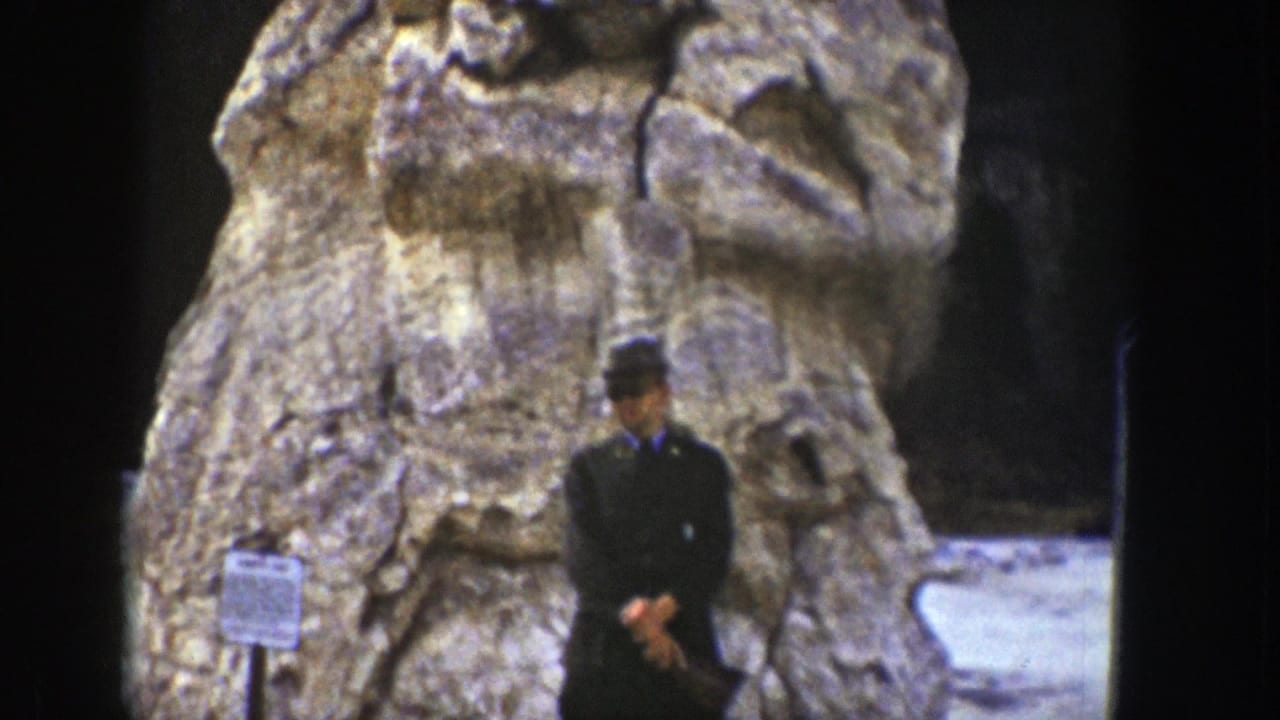 1939 Wyoming frame with a man in dark clothing standing below a weathered carved stone figure.