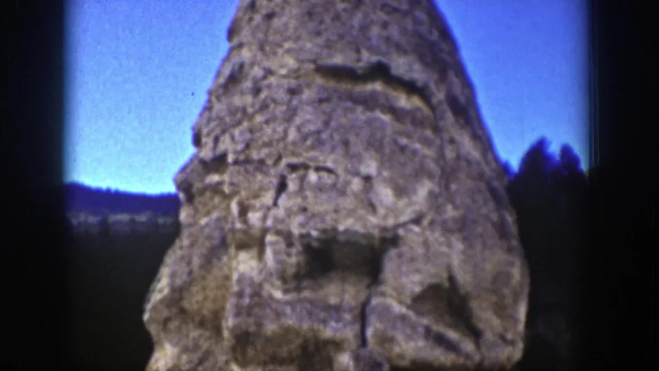 1939 Wyoming home-movie frame looking up at the carved stone monument against a saturated blue sky.