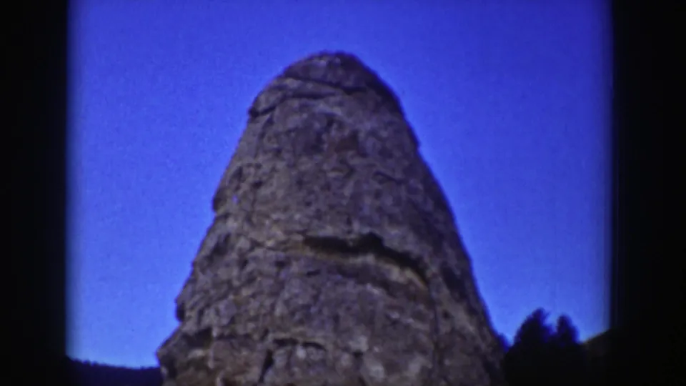 1939 Wyoming frame showing the upper stone carving rising into blue sky, with trees low at the edge.