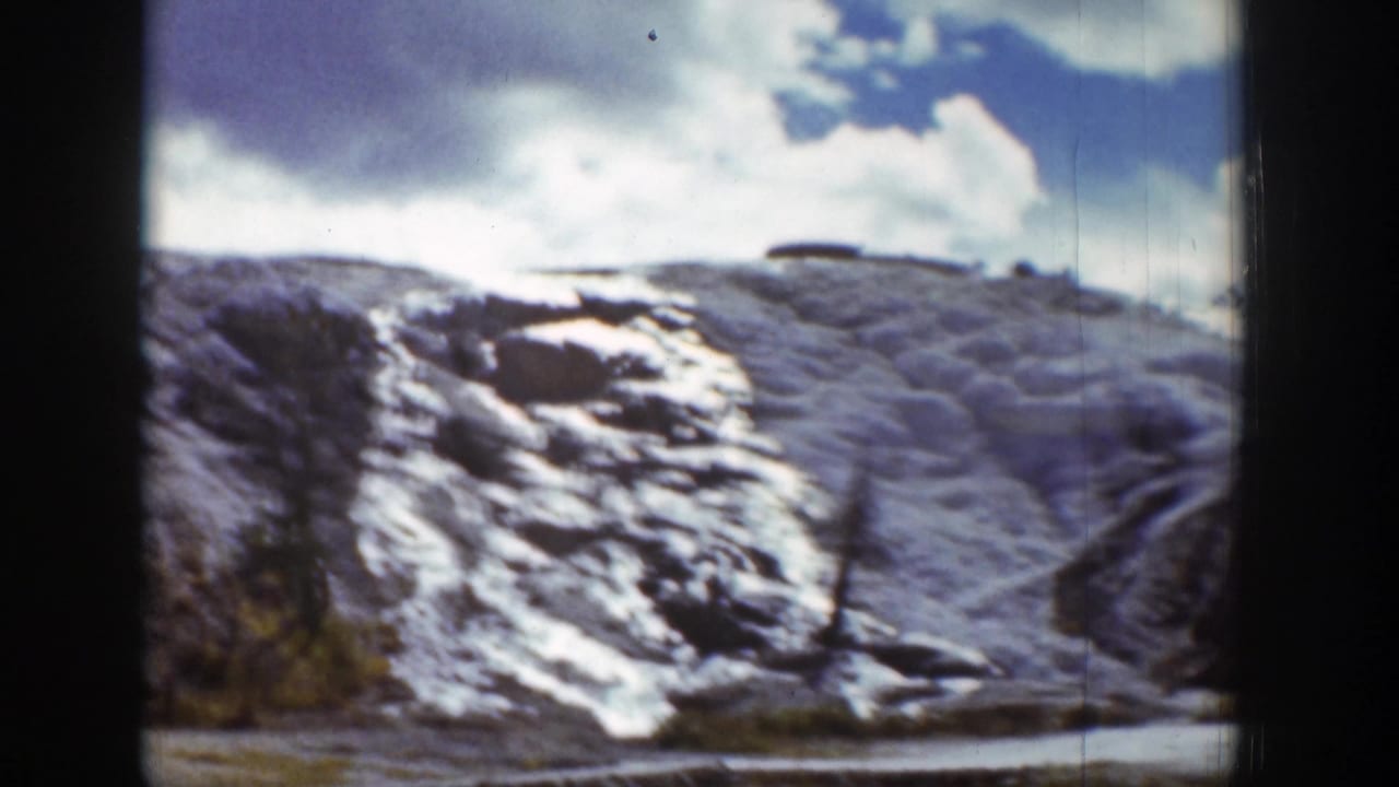 1939 Wyoming home-movie frame of a snow-streaked rocky hillside beneath a bright blue sky and clouds.