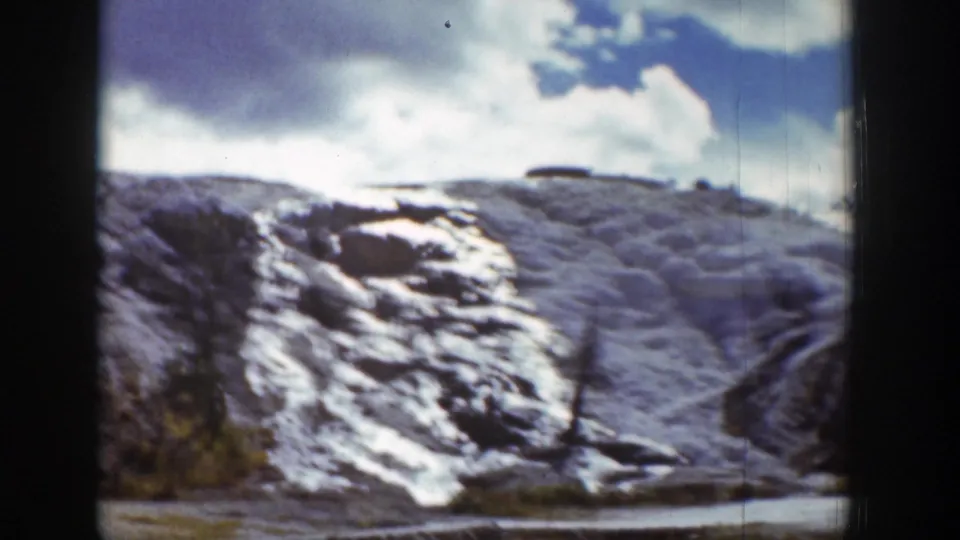 1939 Wyoming home-movie frame of a snow-streaked rocky hillside beneath a bright blue sky and clouds.
