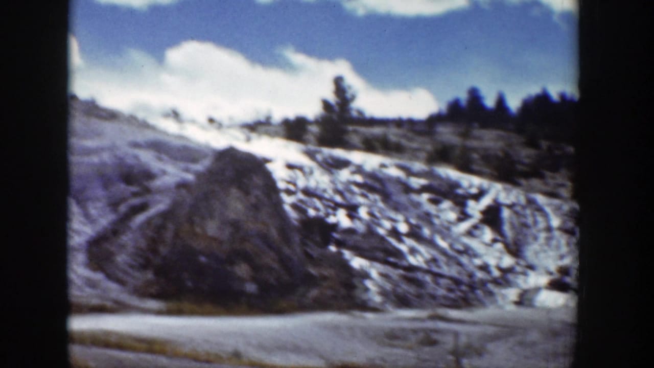 1939 Wyoming frame showing a rocky mound, snow patches, and sparse pine trees on a hillside.