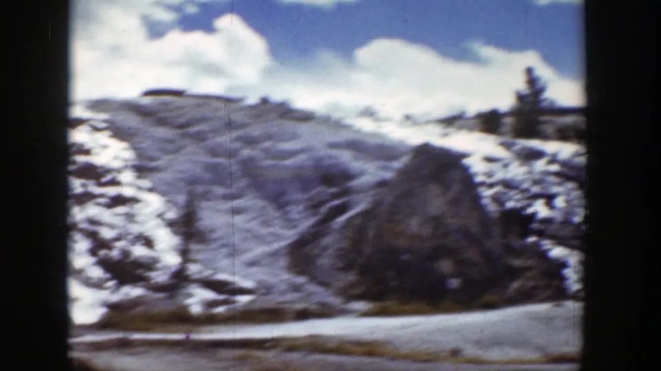 1939 Wyoming home-movie view of a snow-covered slope, large rock, and dirt path in rugged terrain.
