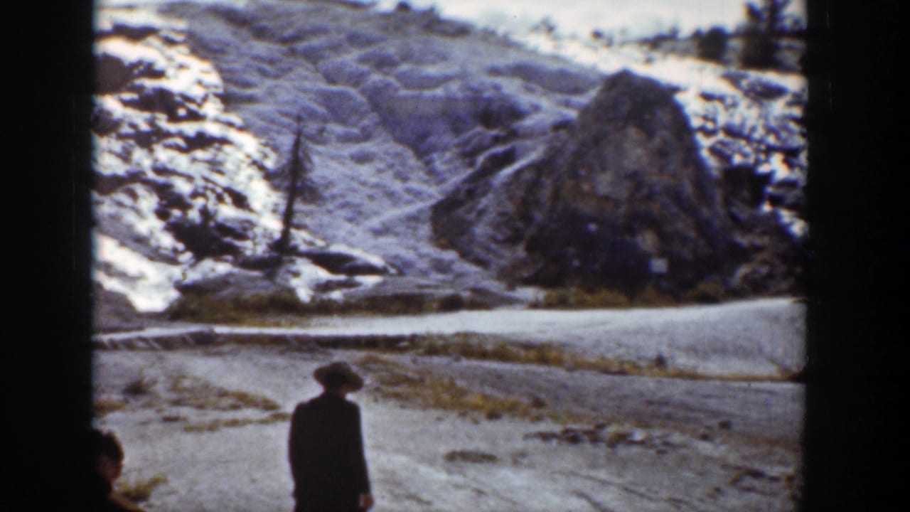 In Wyoming 1939 home-movie footage, a lone bundled figure stands or walks near a snow-covered road beneath rocky winter slopes.