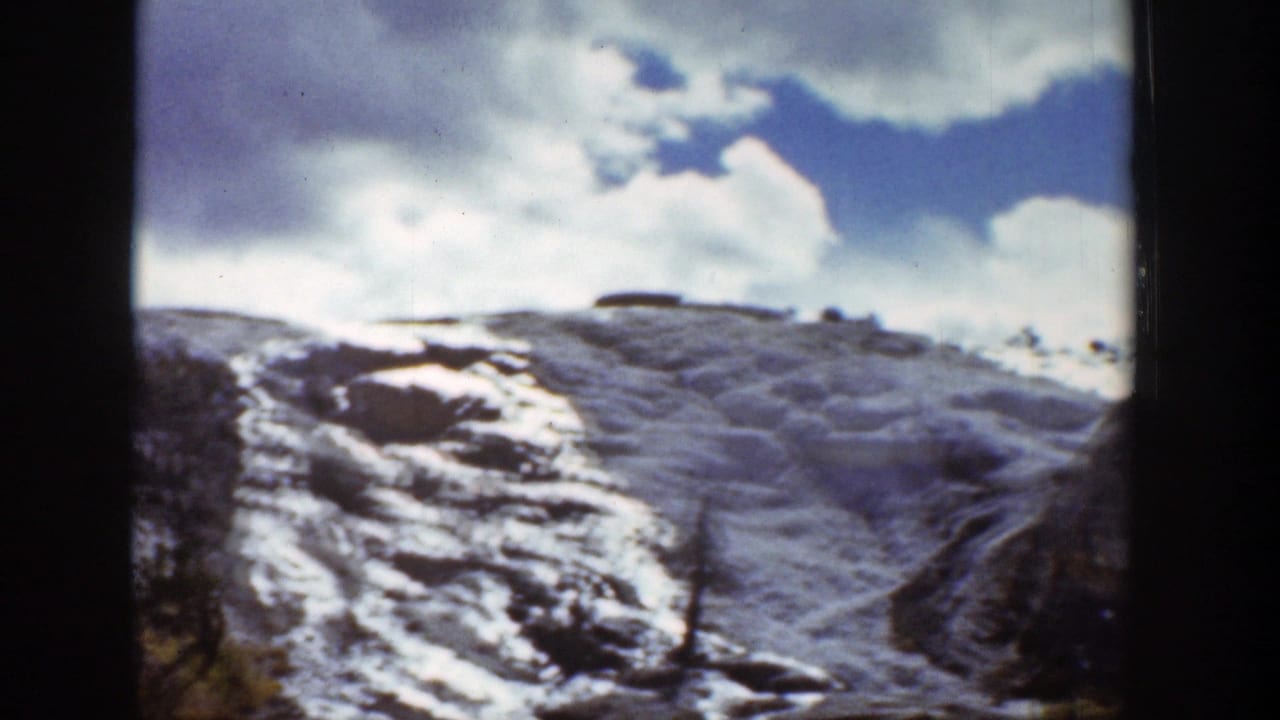 Snow-covered rocky hillside under a cloudy blue sky.